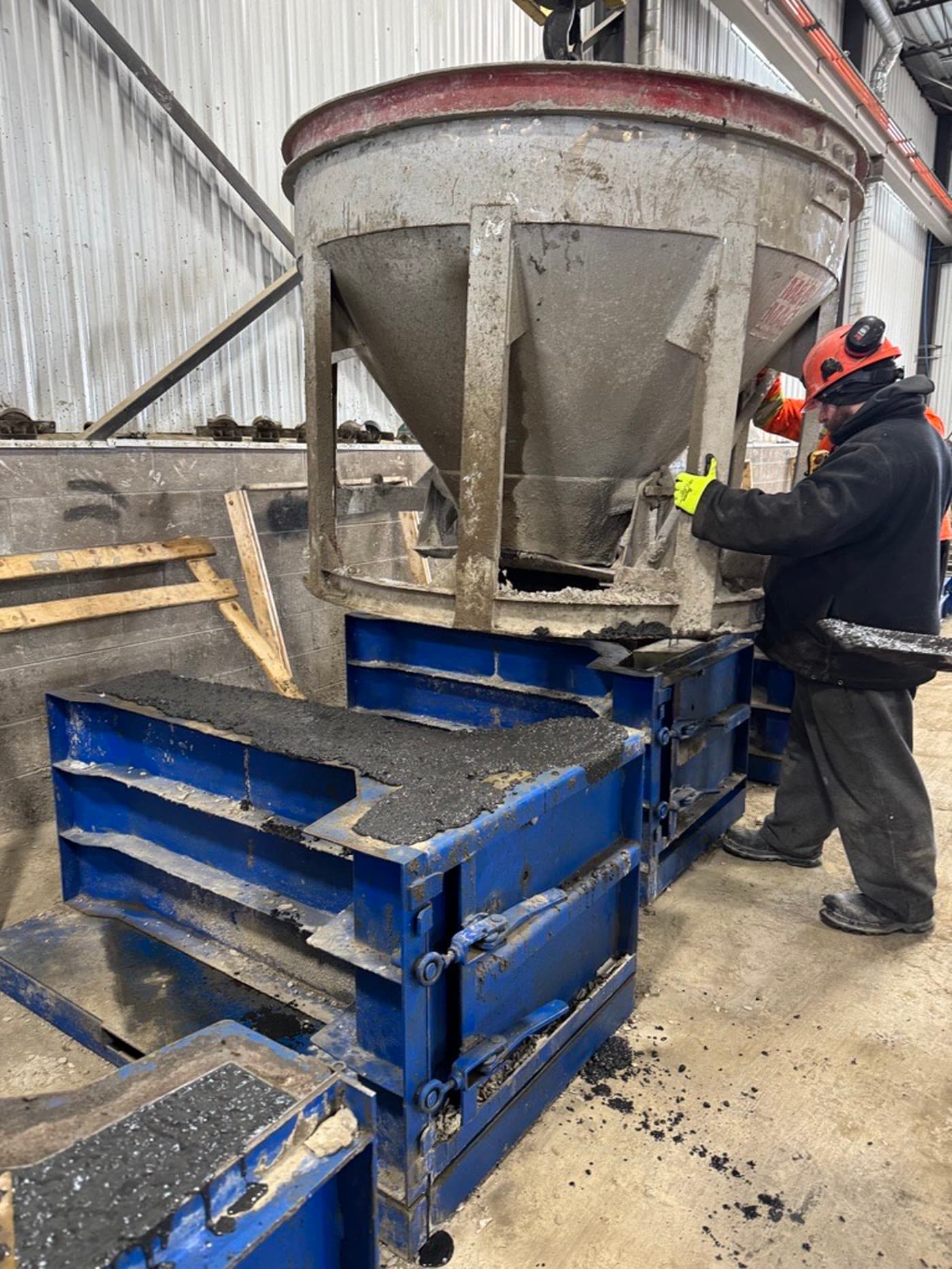 Worker pouring ΔC concrete into blue Magnumstone molds at Casey Concrete plant